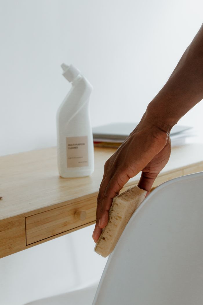 Pièce épurée où une personne nettoie une chaise avec une éponge et un produit d’entretien.